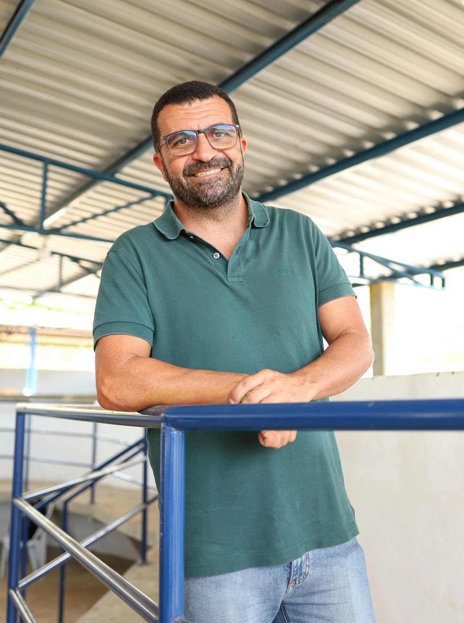 Abinho Neme sorri apoiado no guarda-corpo azul de um galpão