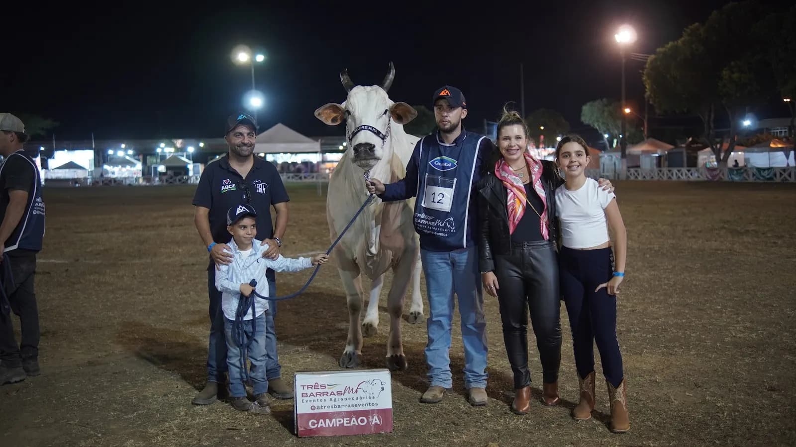Criadores e família com a vaca campeã e a placa de premiação na pista, à noite, na 65ª ExpoAgro